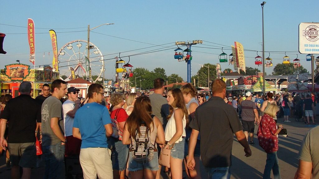 Historical Illinois State Fair scene with visitors, food stands, a Ferris wheel, and overhead Sky Glide chairs